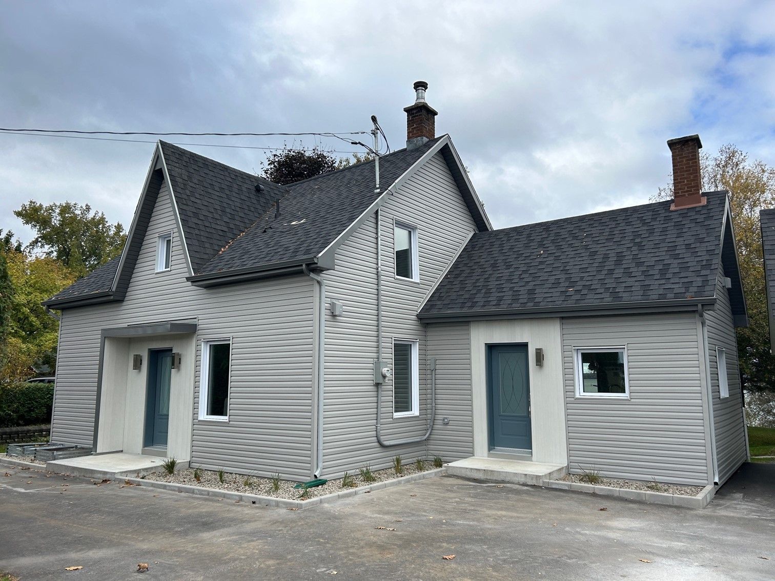 Maison grise avec deux cheminées, toit foncé et deux portes bleues.