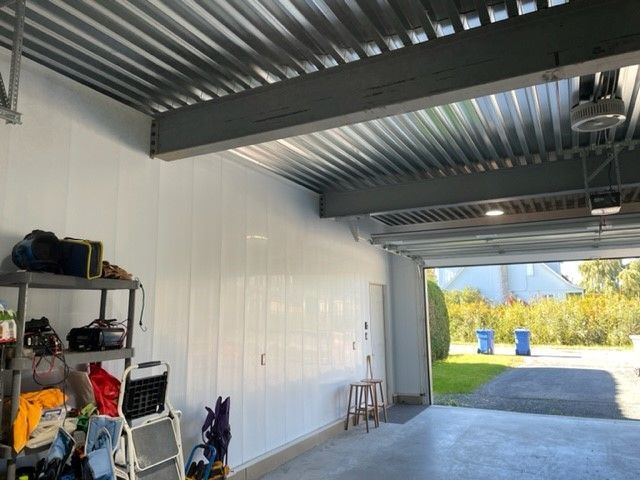 Intérieur du garage avec murs en panneaux blancs, toit en métal et porte de garage ouverte.