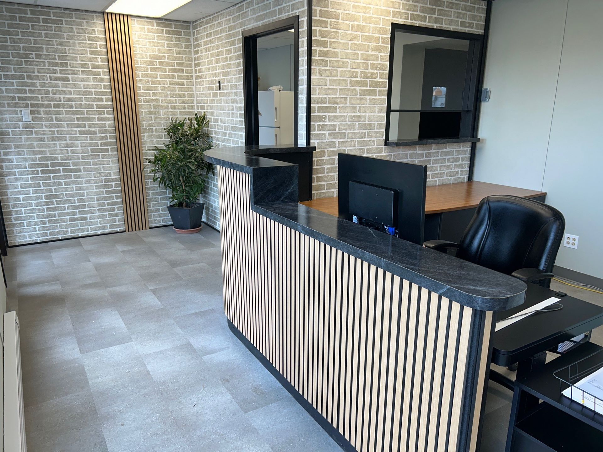 Espace de réception avec comptoir rayé, murs en briques grises et bureau.