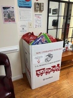 A box filled with toys for tots is sitting on a wooden floor in a room.
