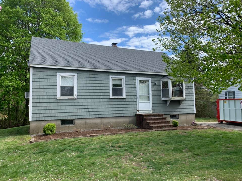 A small house with a gray siding and a gray roof is sitting in the middle of a lush green field.