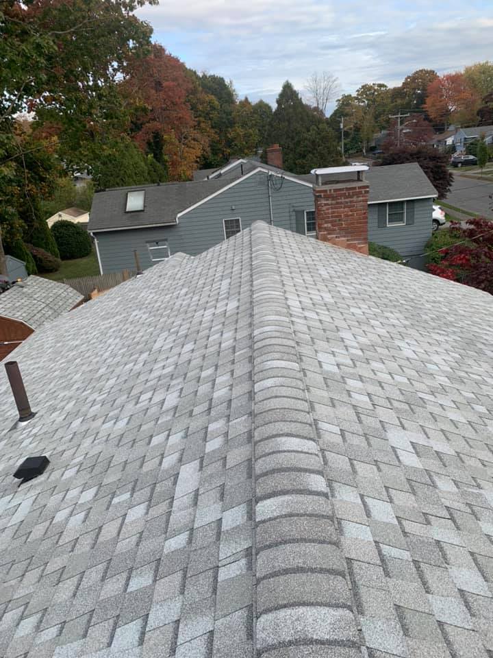 The roof of a house with a gray shingle roof and a chimney.