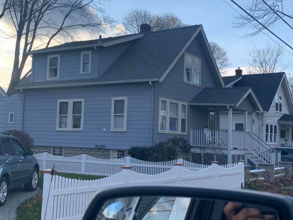 A car is parked in front of a house with a white picket fence.