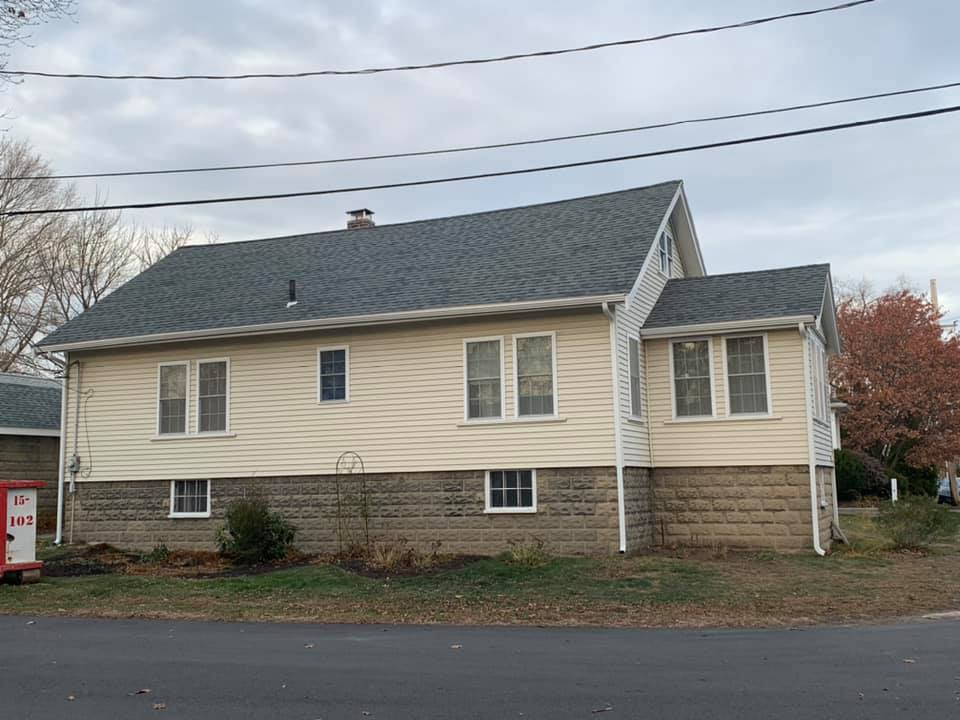 A house with a gray roof and white siding is sitting on the side of the road.