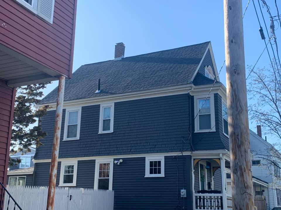 A black house with a white fence and a chimney on the roof.
