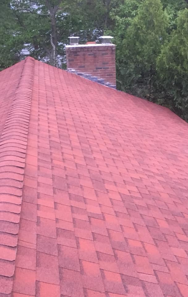 A close up of a red roof with a chimney in the background.