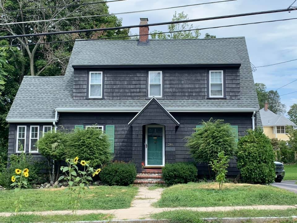 A black house with a gray roof and green shutters