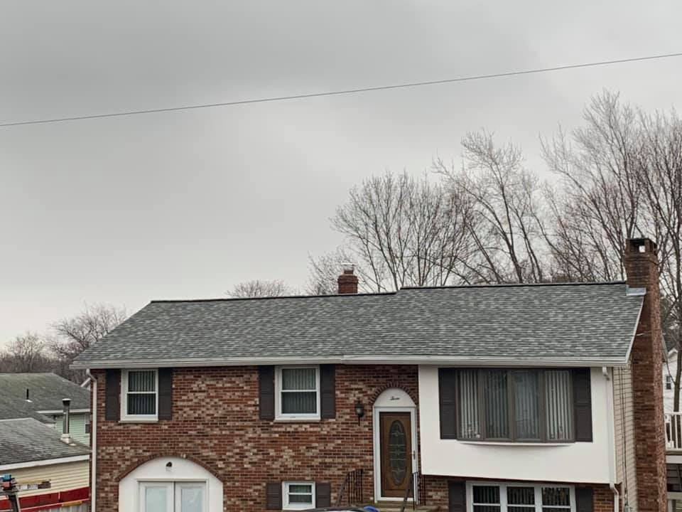 A brick house with a gray roof and black shutters on a cloudy day.
