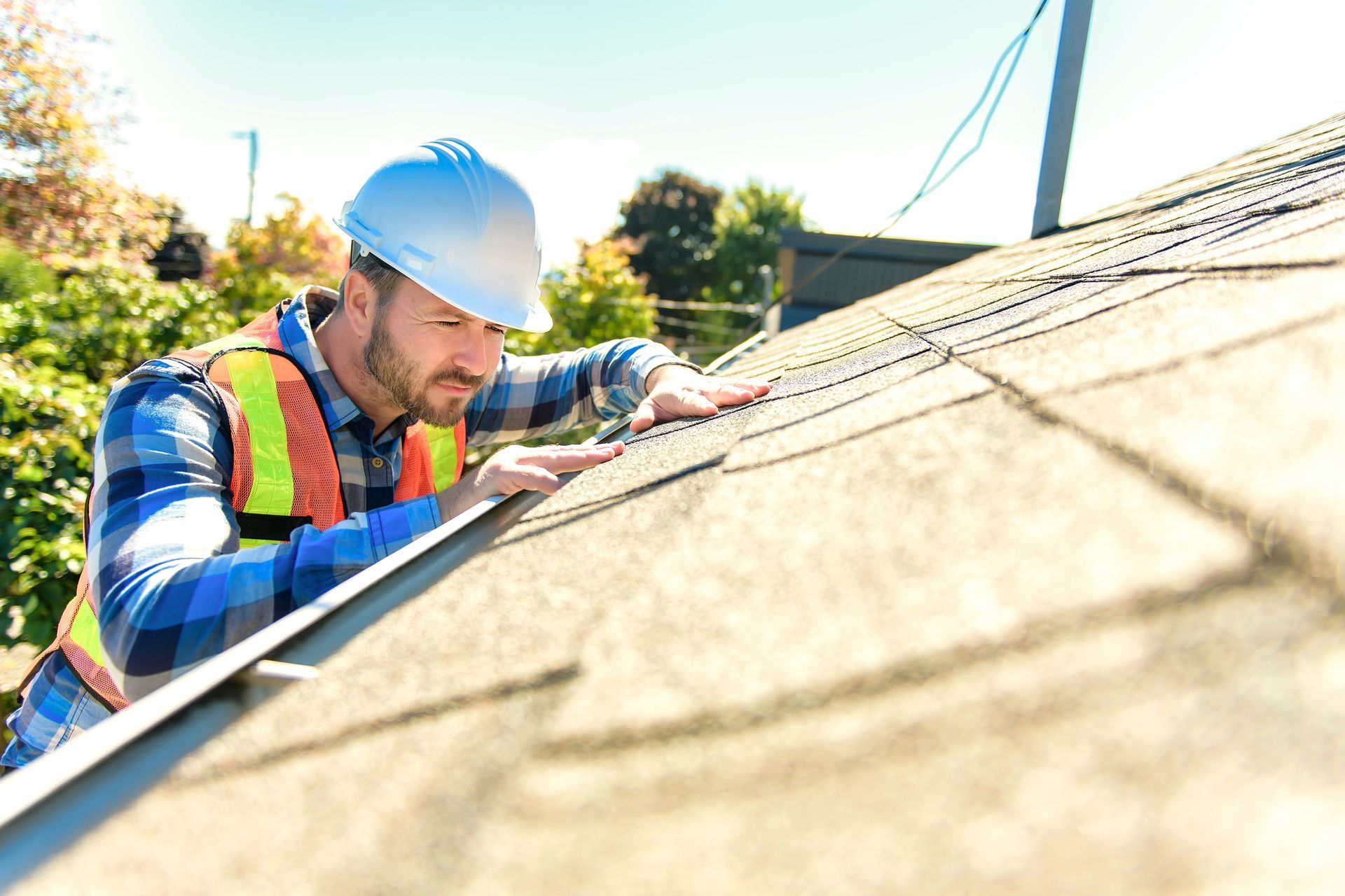 A man wearing a hard hat and safety vest is working on a roof.