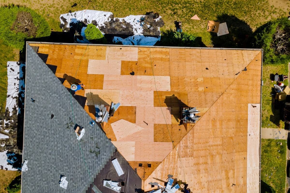 A man is kneeling on top of a roof looking at solar panels.