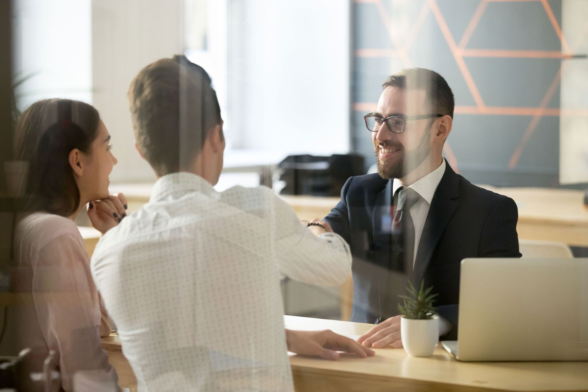 Couple consults with a smiling financial advisor at a desk in a modern office.