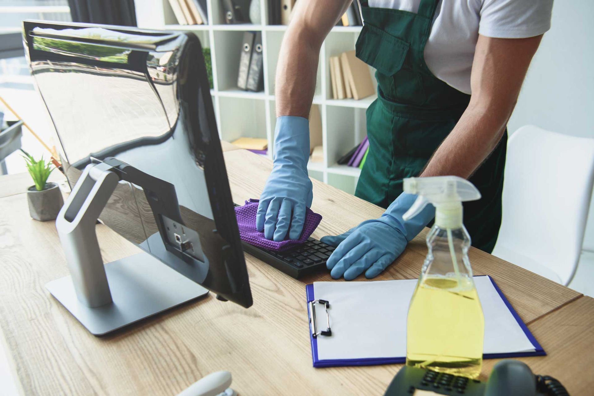 Person wearing gloves cleaning a computer keyboard with spray bottle on desk. Person wearing gloves cleaning a computer keyboard with spray bottle on desk.