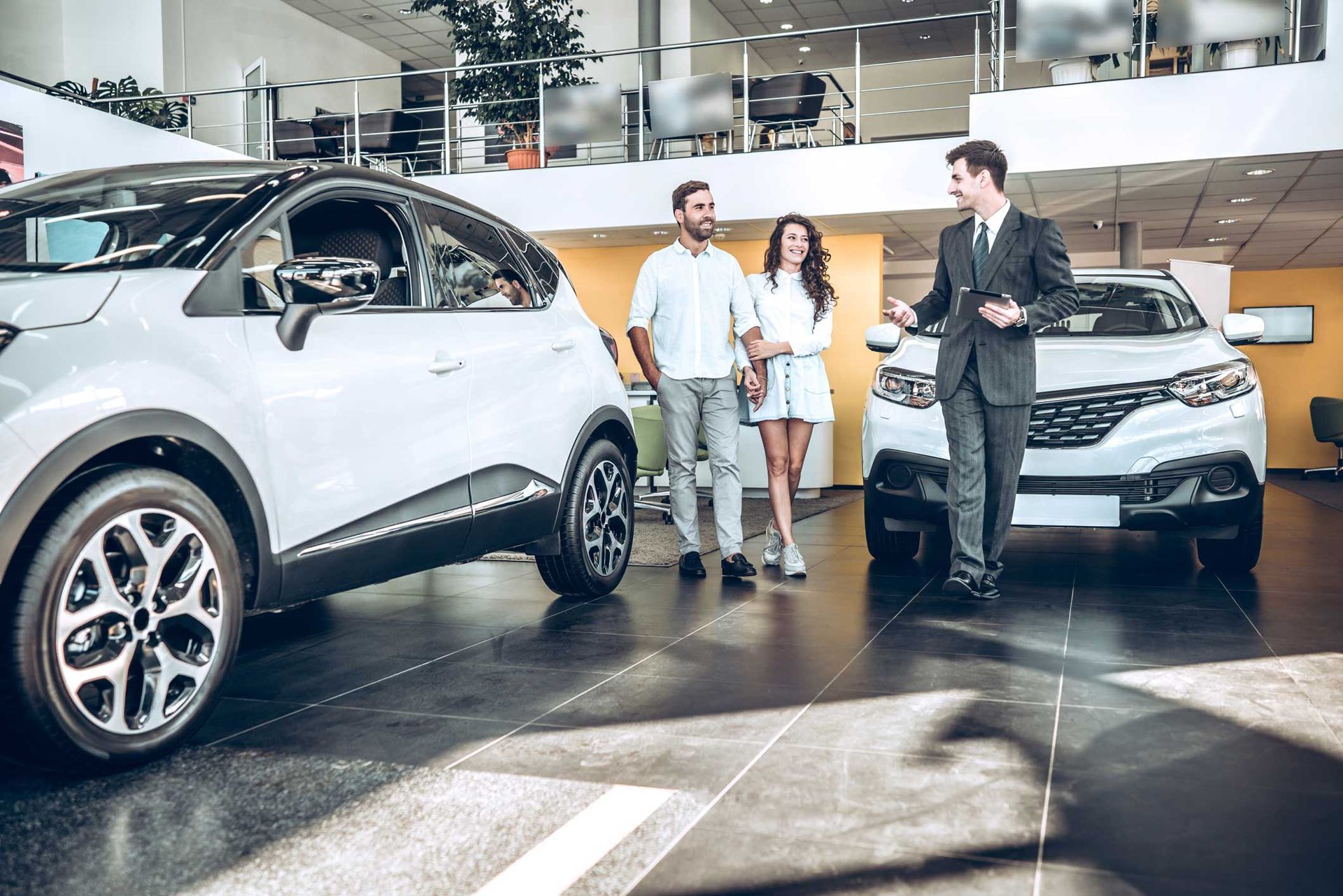 Couple with salesperson in car showroom, looking at vehicles.
