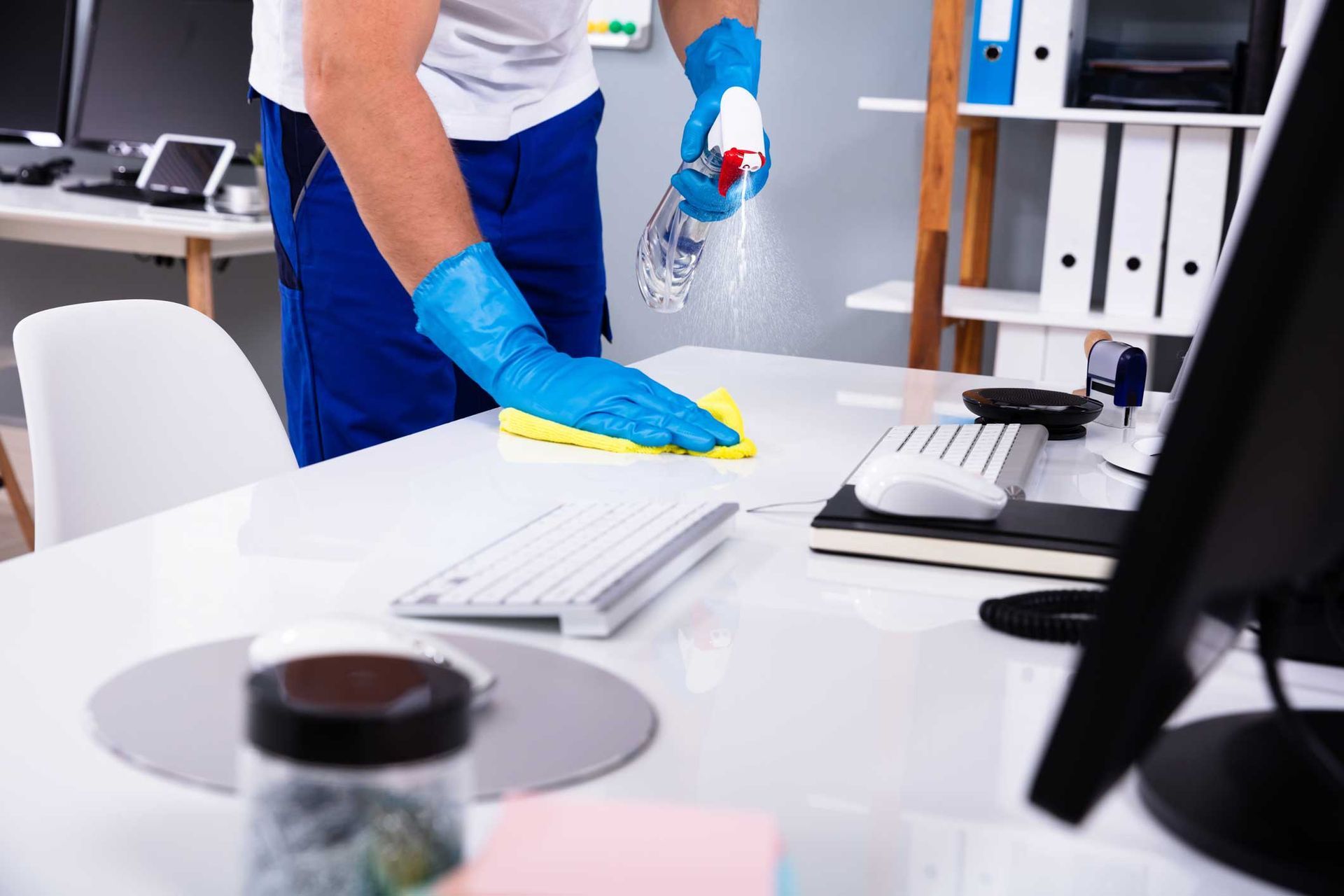 Person cleaning an office desk with spray bottle and yellow cloth. Person cleaning an office desk with spray bottle and yellow cloth.