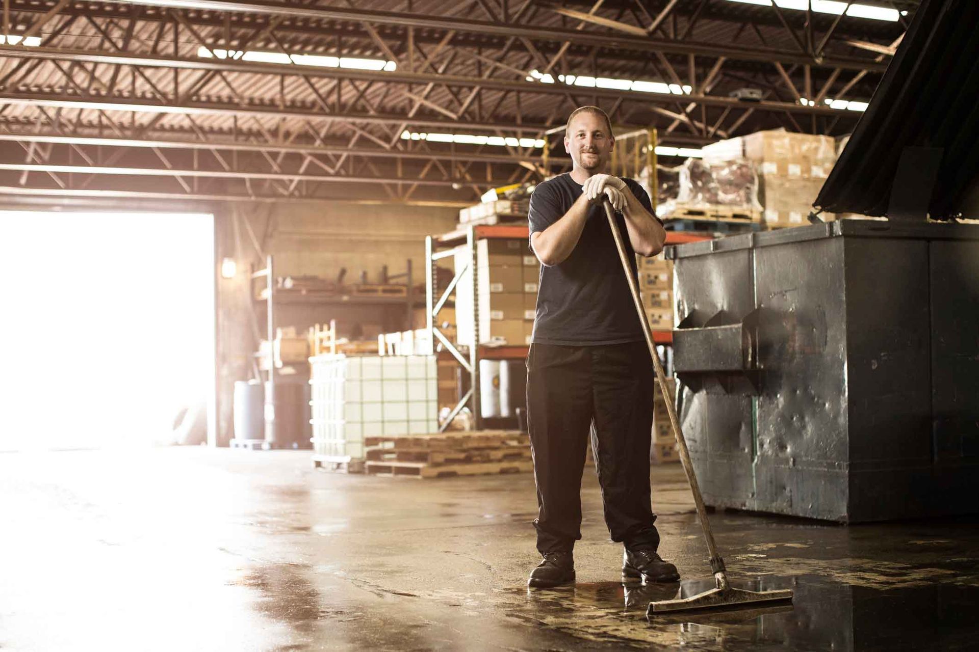 Man mopping a warehouse floor. Sunlight streams in. Boxes and equipment are in the background. Man mopping a warehouse floor. Sunlight streams in. Boxes and equipment are in the background.