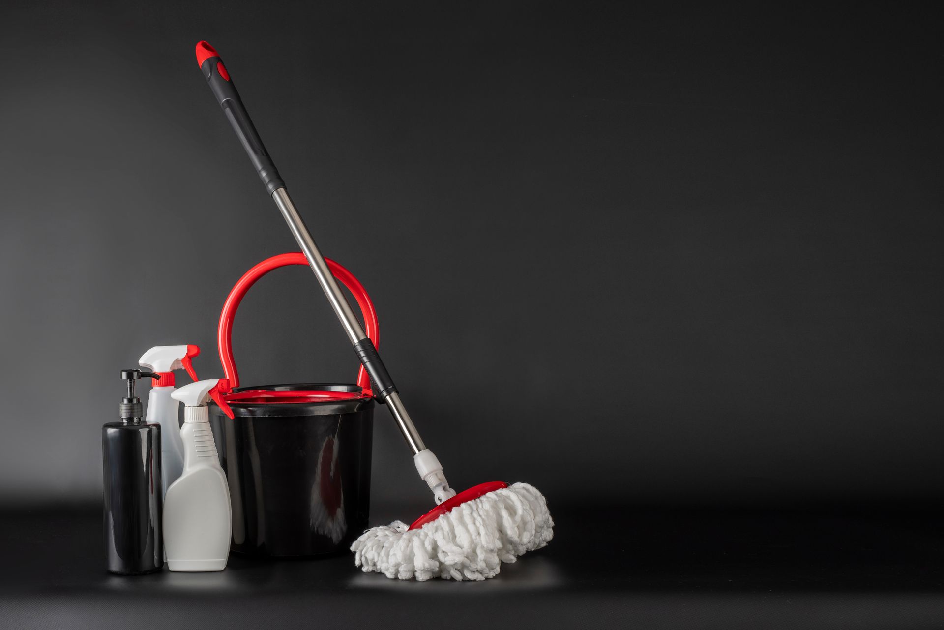 Red-and-white mop, bucket, and cleaning supplies on a dark background
