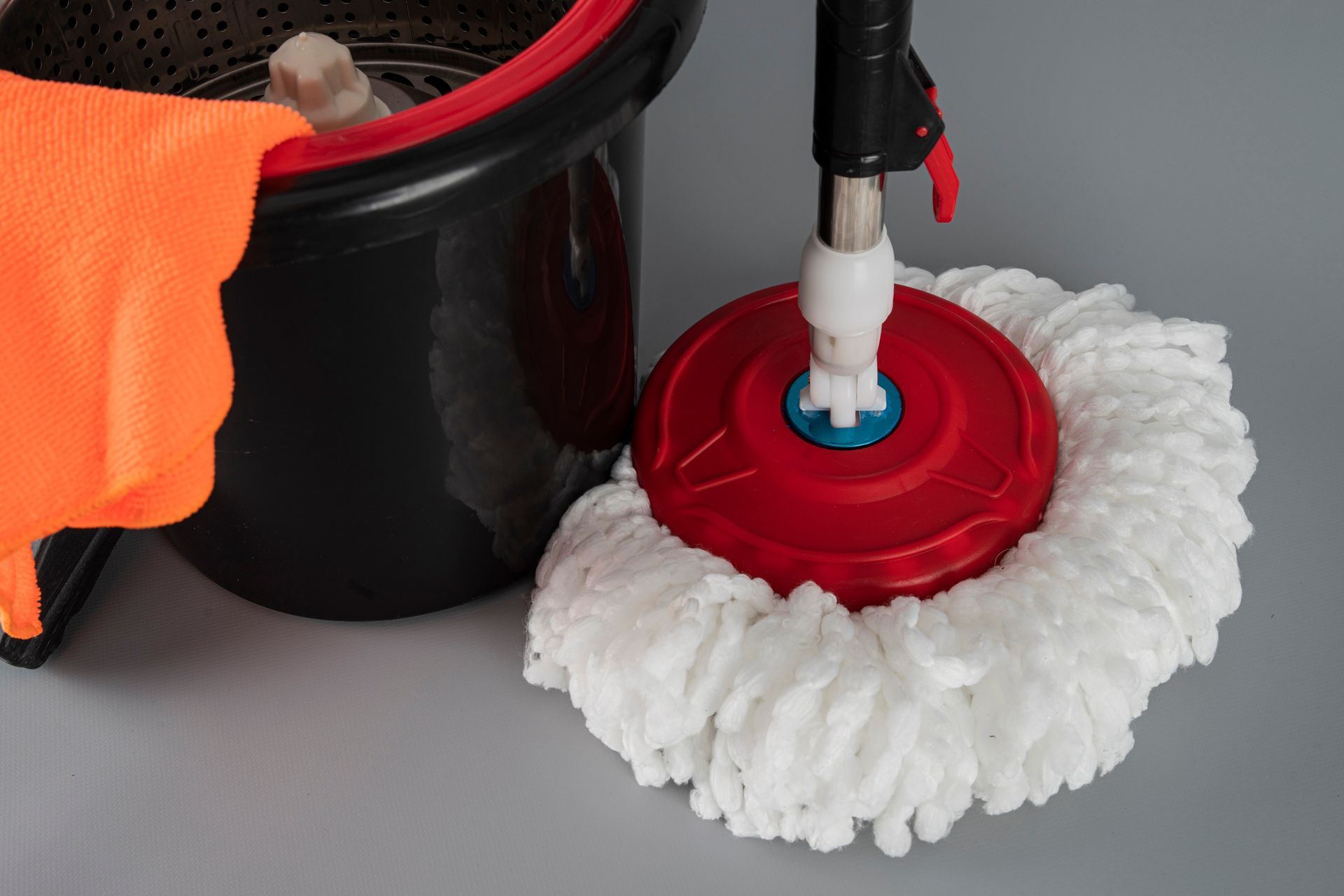 Red spin mop head beside a black bucket with an orange cleaning cloth