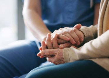 A nurse is holding the hands of an elderly woman.