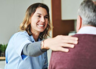 A nurse is hugging an elderly man and smiling.