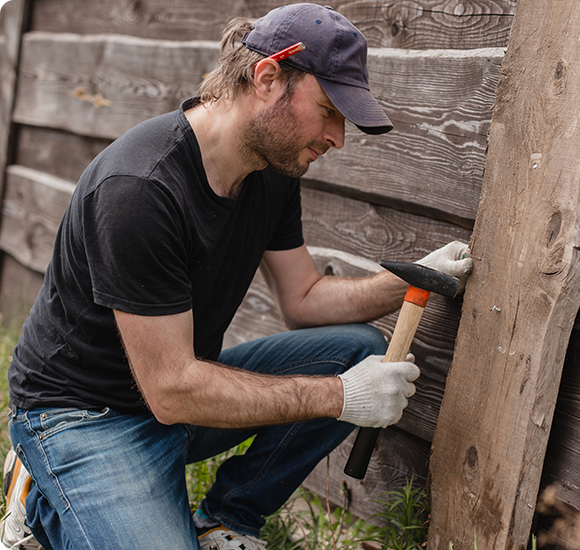 a man is kneeling down holding a hammer against a wooden wall .