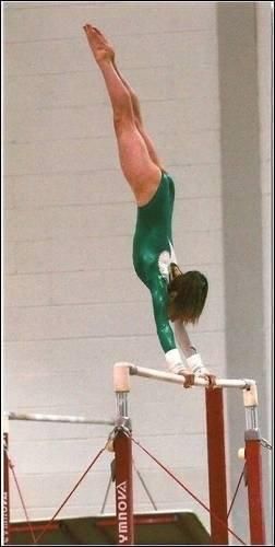 Lauren Lethbridge in a green and white leotard doing a handstand on the top of the bars