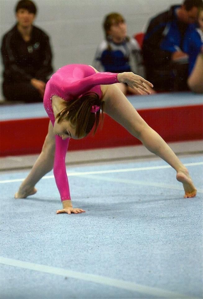 Lauren Lethbridge in a pink leotard is bent over backward and one hand on the floor position.