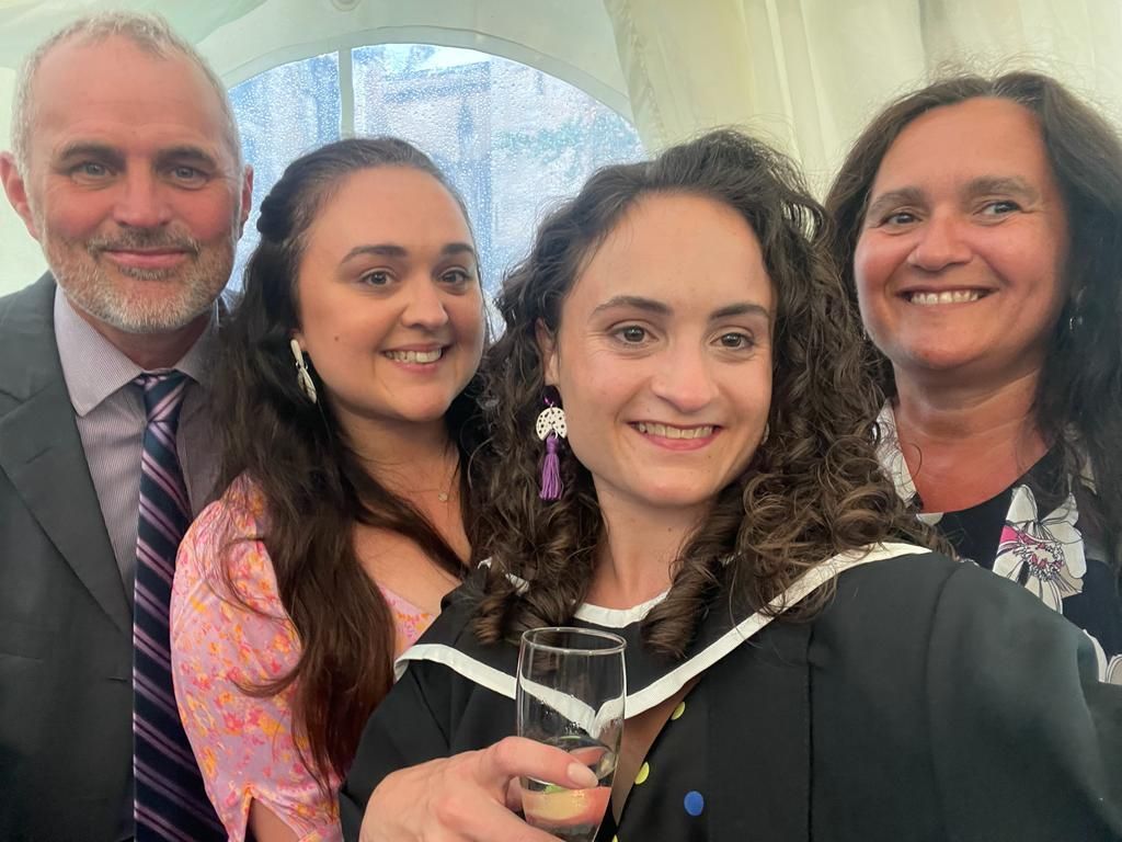 Lauren Lethbridge in her black graduation gown with a black hood edged in white with her dad to the far left in a grey suit with a lilac shirt and blue and lilac tie. Between Lauren and her dad is her sister who is wearing a floral top and white earing with dark long hair. To the right of Lauren is her mumwhi has a black patterned top on with long dark hair. 