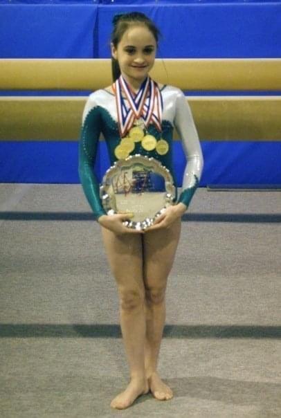 Lauren Lethbridge in a green and white leotard with five gold medals around her neck and holding a silver plate. 