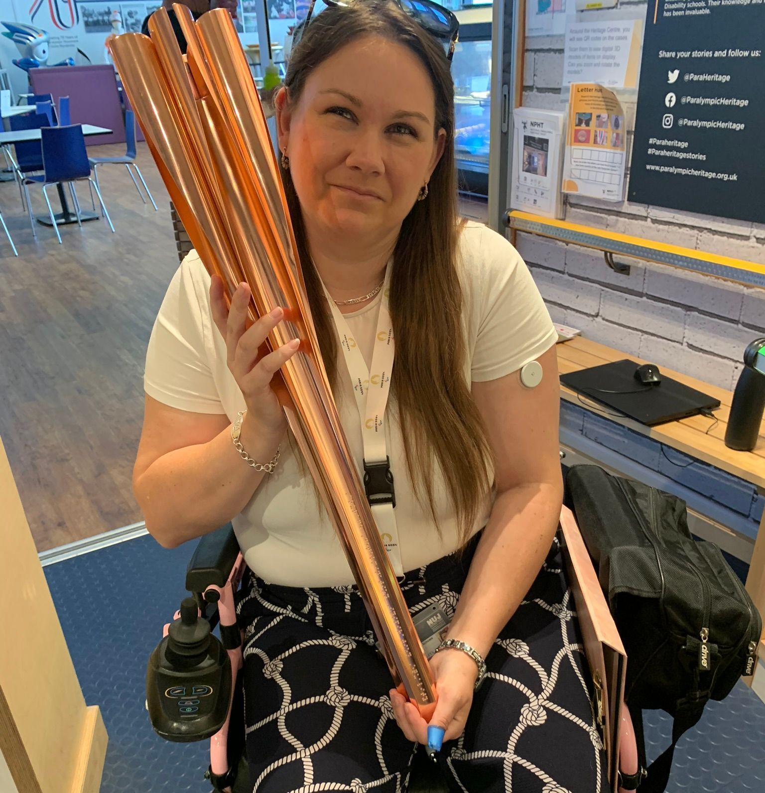 Victoria-Jayne with the Tokyo 2020 Paralympic flame, wearing a white t-shirt, blue and white trousers, and sitting in her wheelchair.
