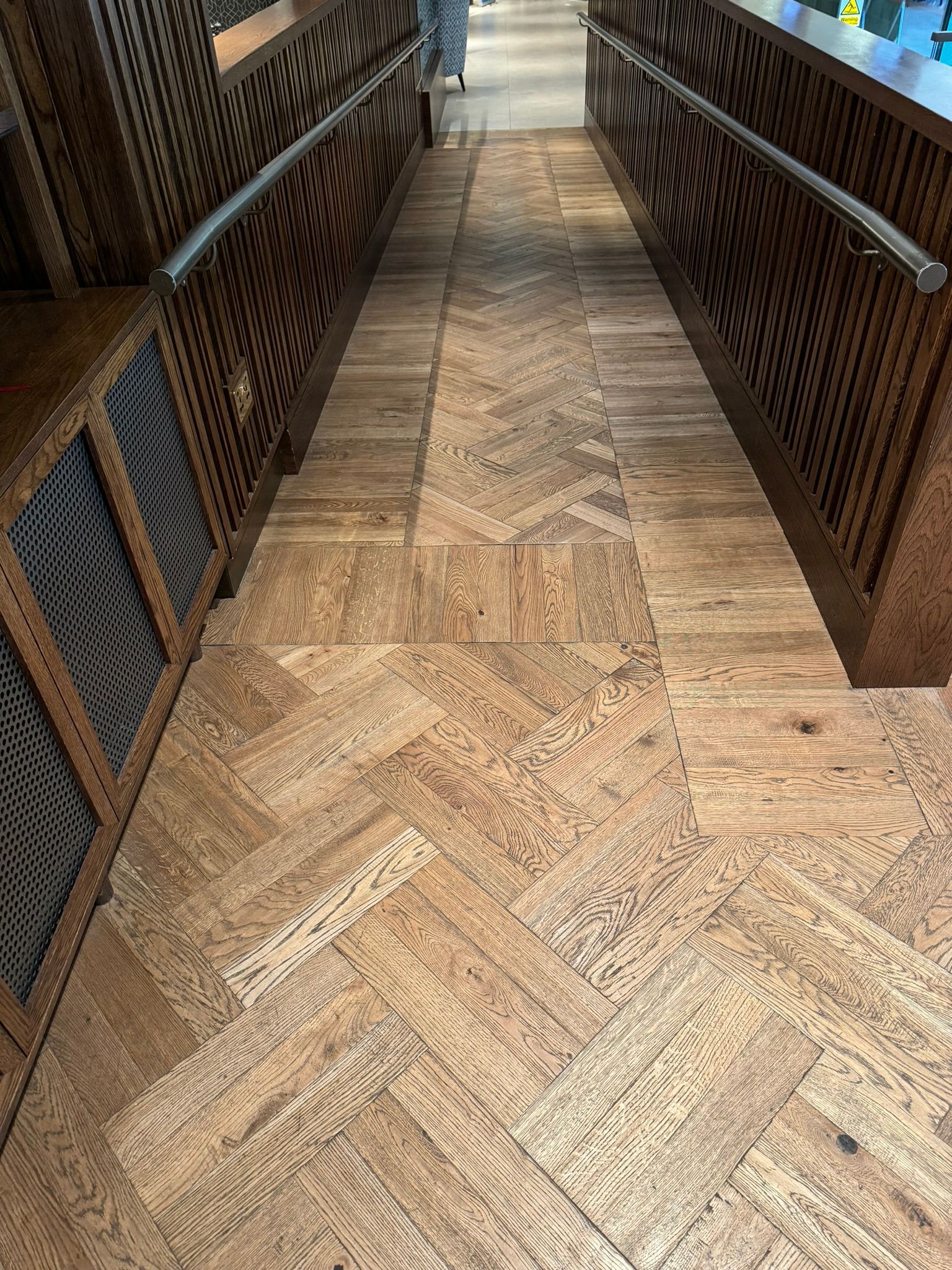 Wooden floor board with mahogany-style panelled walls with handrails on either side. 