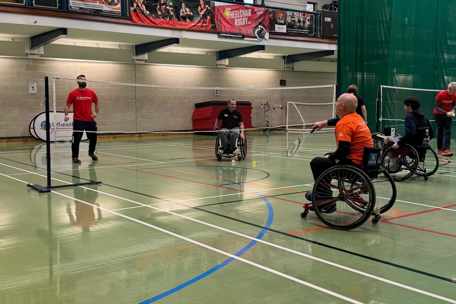 Badminton court with wheelchair users and non-disabled participants taking part in a game of badminton. 