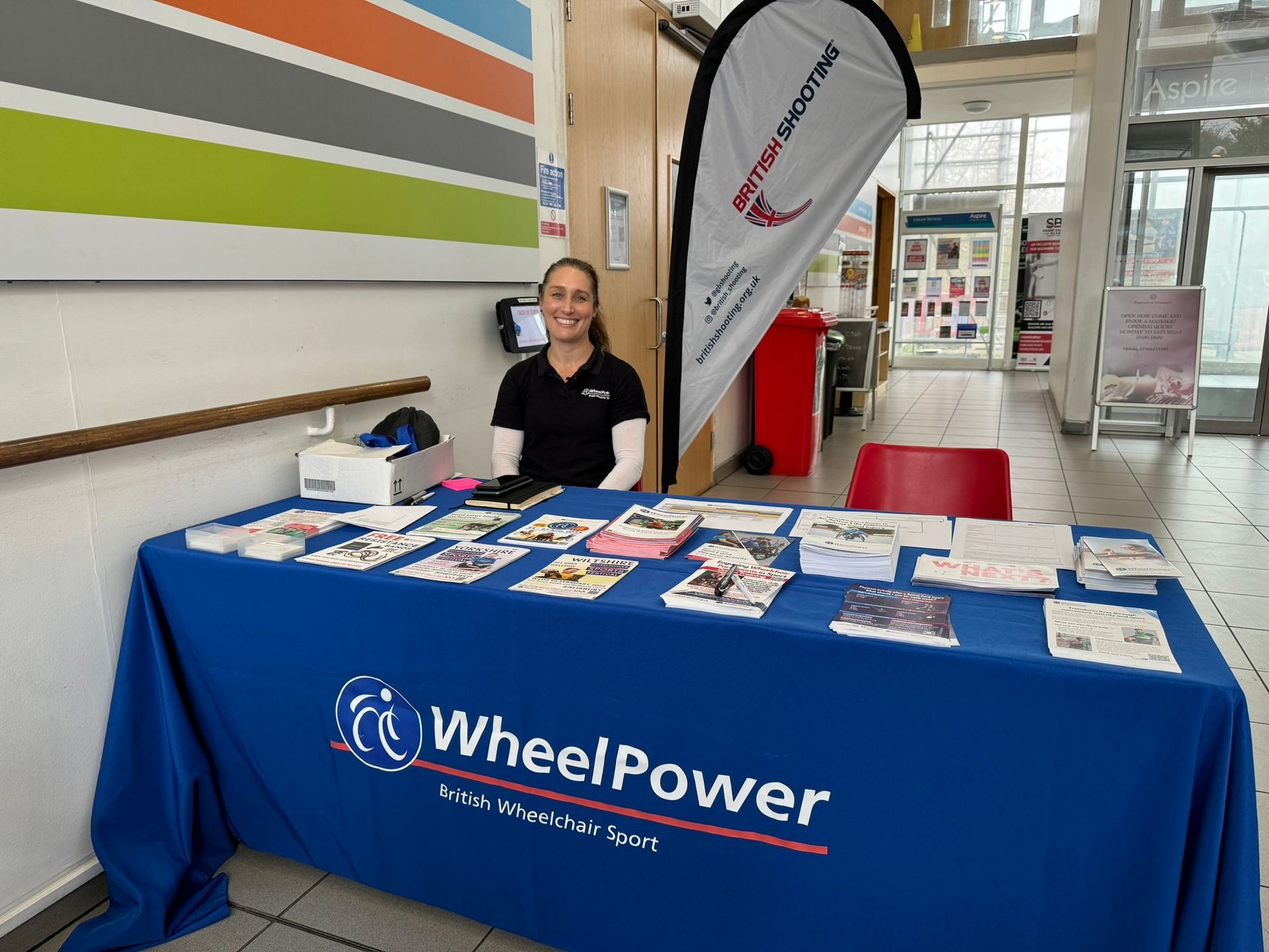 WheelPower stall with leaflets about the organistation. Ella sits behind the desk. 