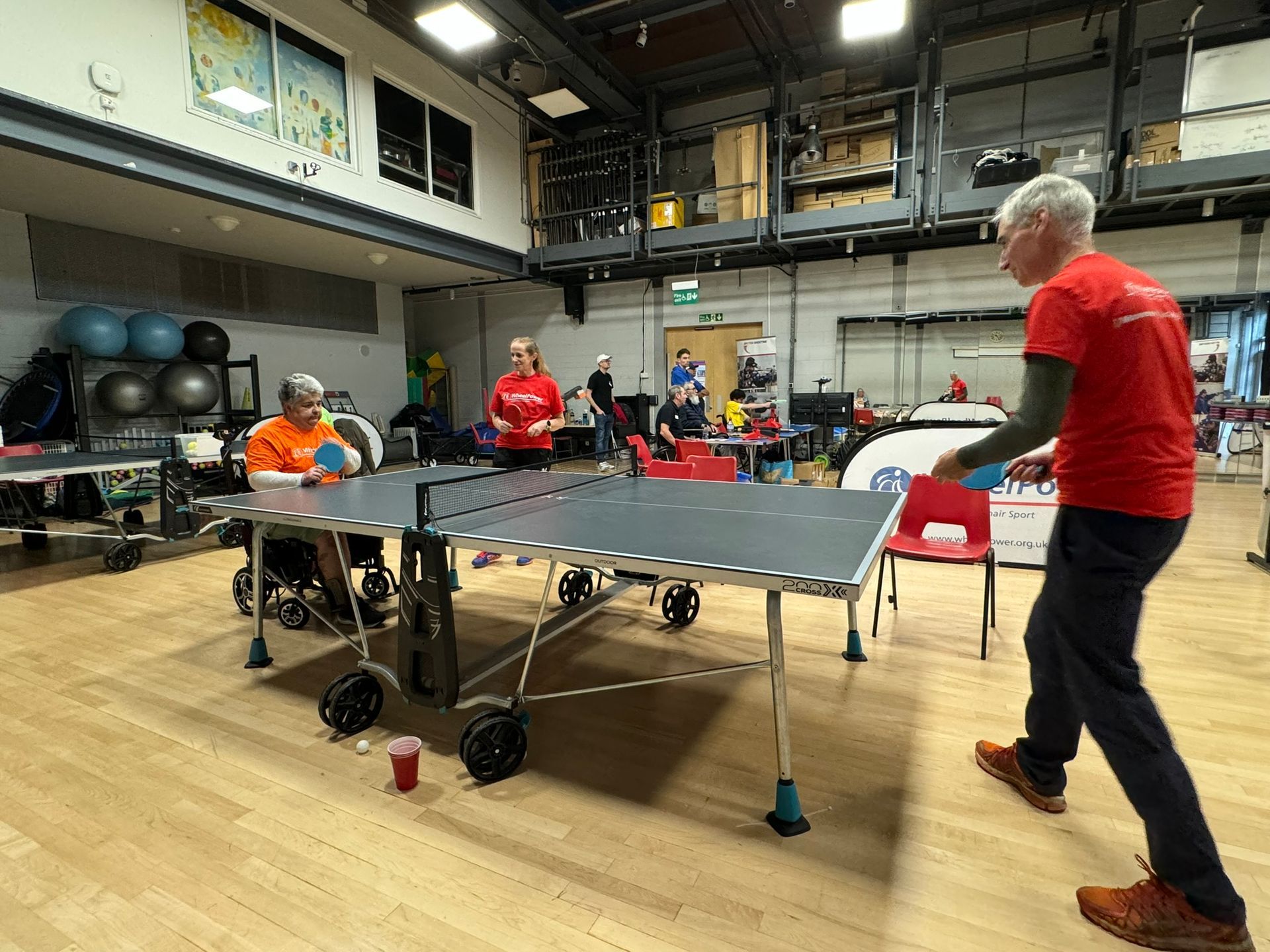 Table tennis match between participant and volunteer. One is sitting one is standing. 