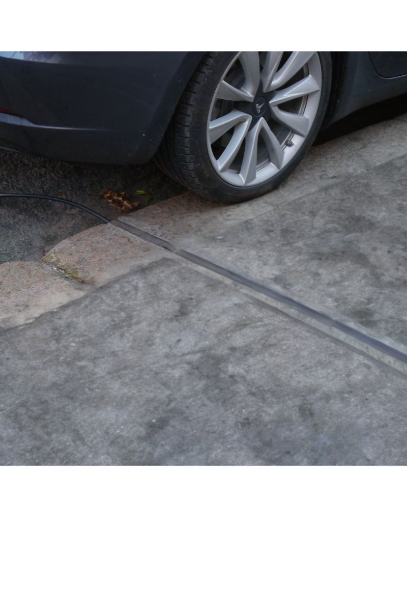 grey pathway with cable gully running through it and a car at back with rear-wheel on pavement