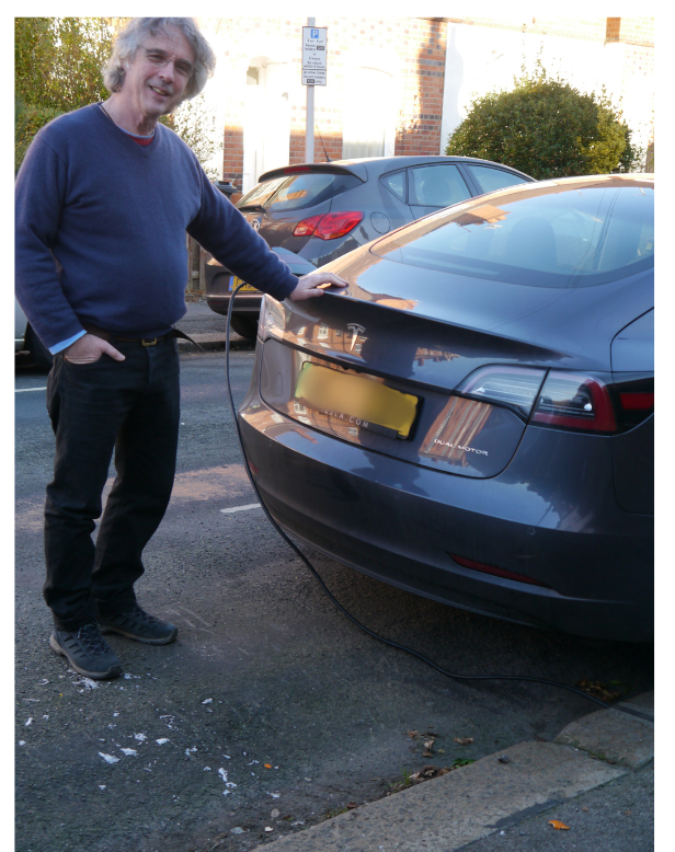 Tim Liddle with hand on his Tesla car with Ev Cable running from Kerbo charge gully to the car. 