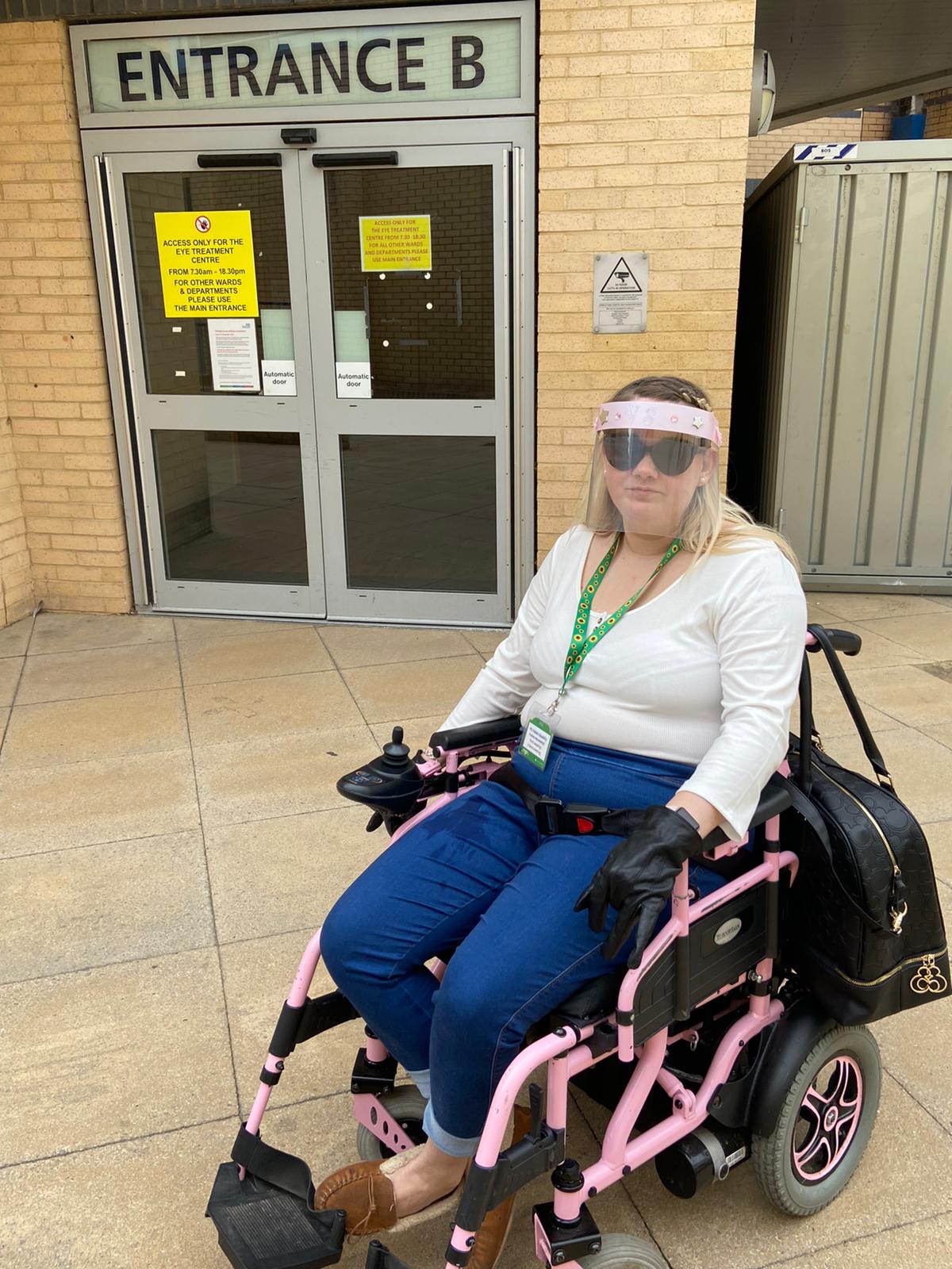 Victoria-Jayne Sat in her powerchair outside the entrance to a hospital.