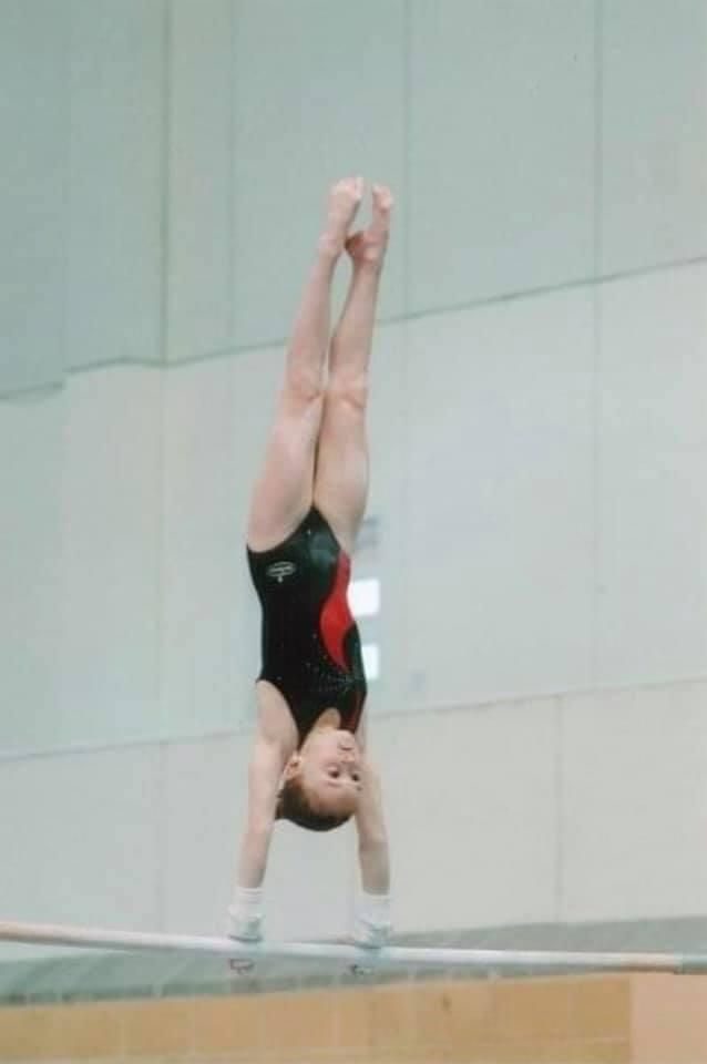 Lauren Lethbridge in a black leotard with a red stripe doing a handstand on the bars