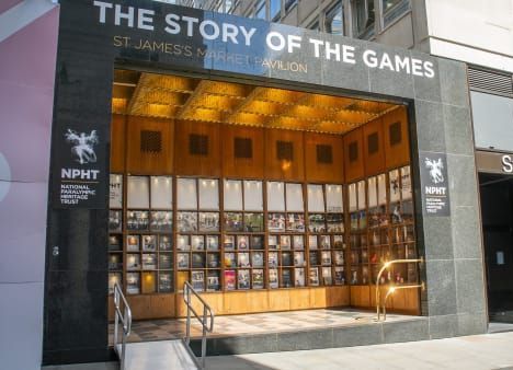 outside of a building with the words Story of the games on the outside, metal bars create a ramp up to an exhibition of books behind glass