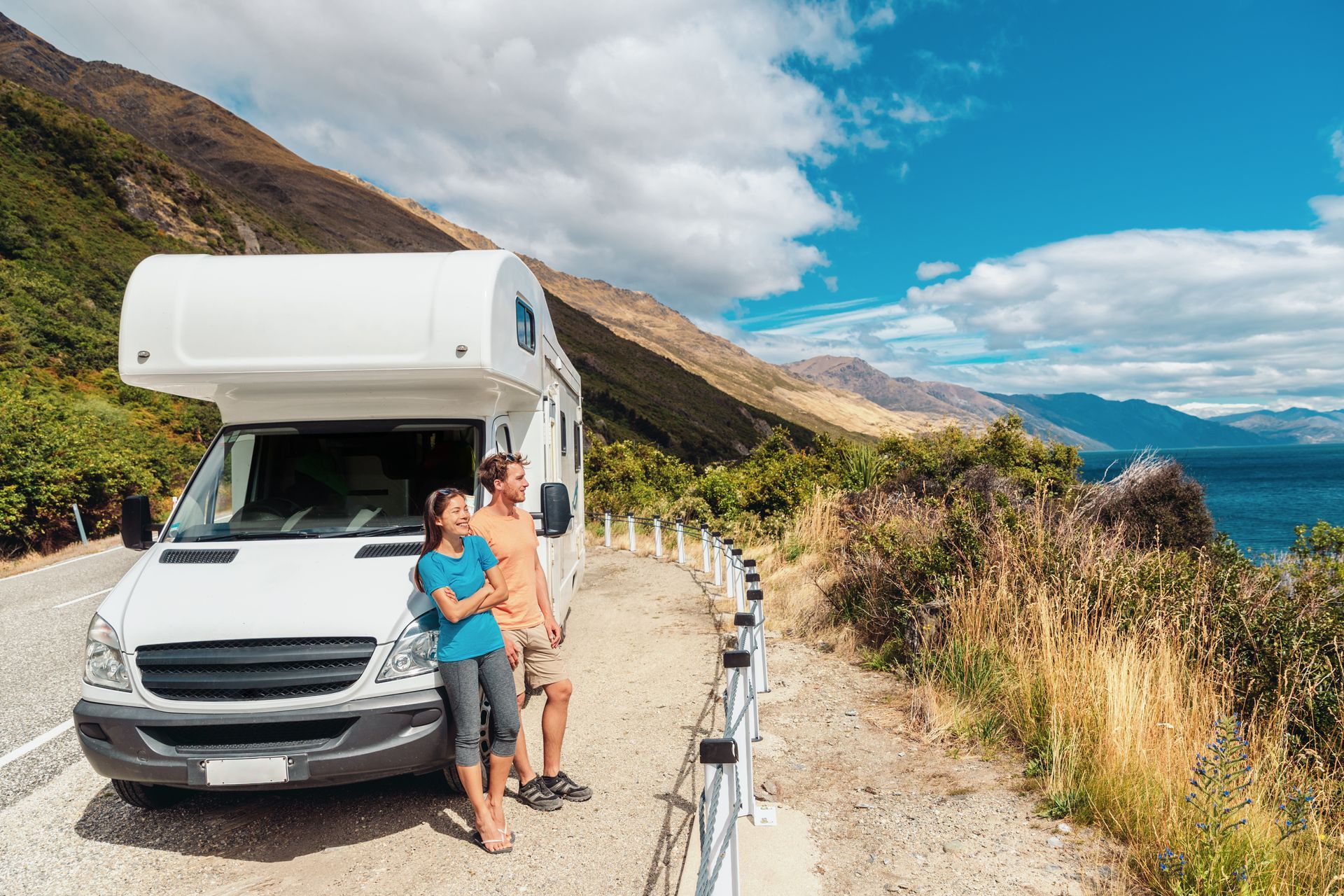 A couple on vacation looking at a mountain landscape while standing on their motorhome RV camper.