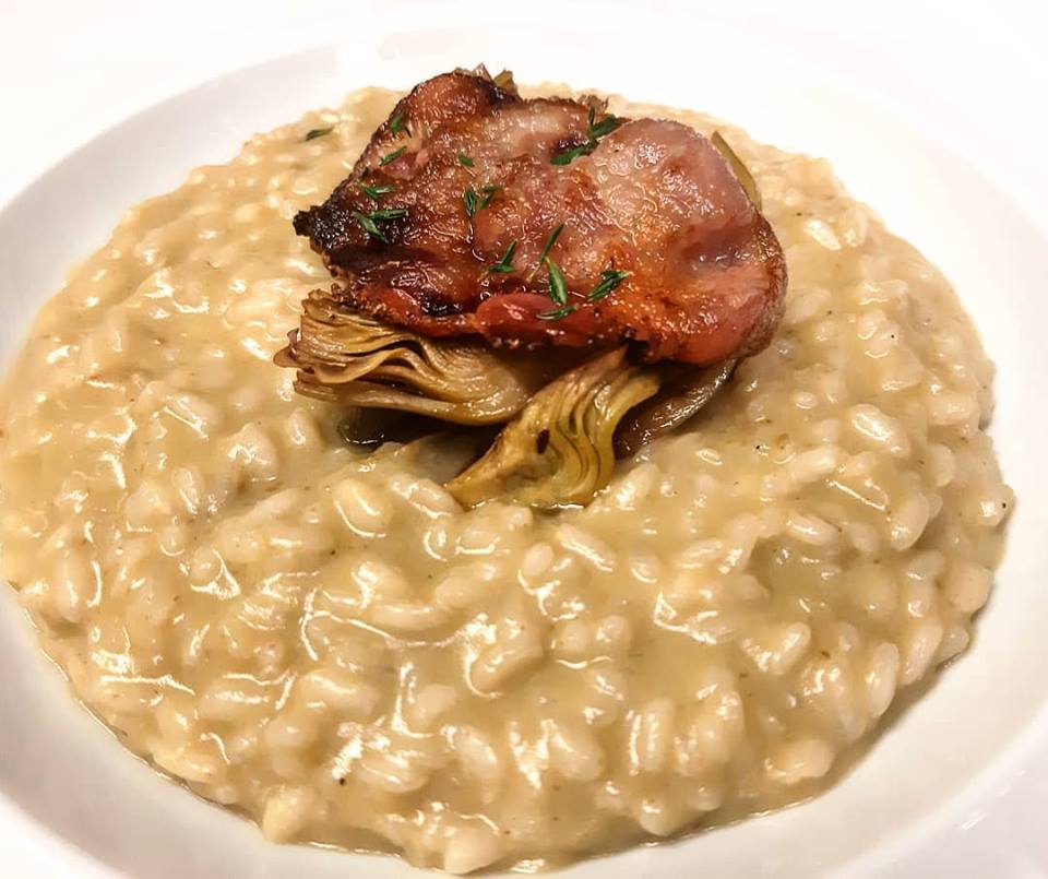 Un piatto di risotto con carciofi e pancetta sopra.