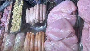 A variety of meats and sausages are displayed on a shelf in a butcher shop.