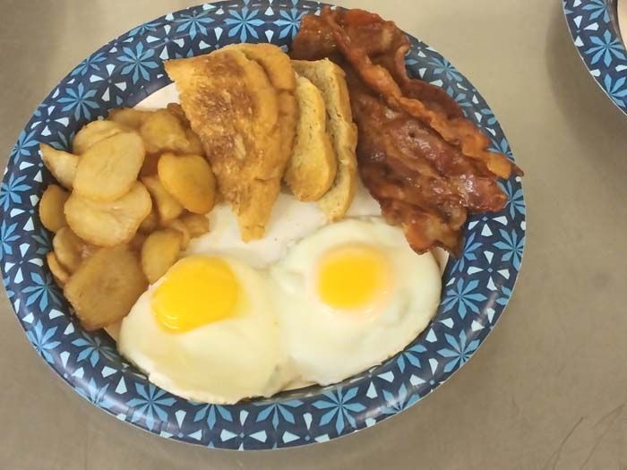 A paper plate with eggs bacon and french fries on it