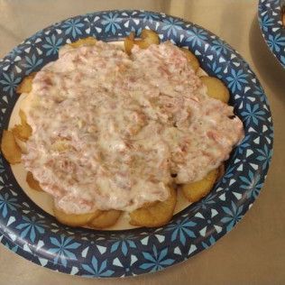 A paper plate topped with french fries and a sauce on a table.