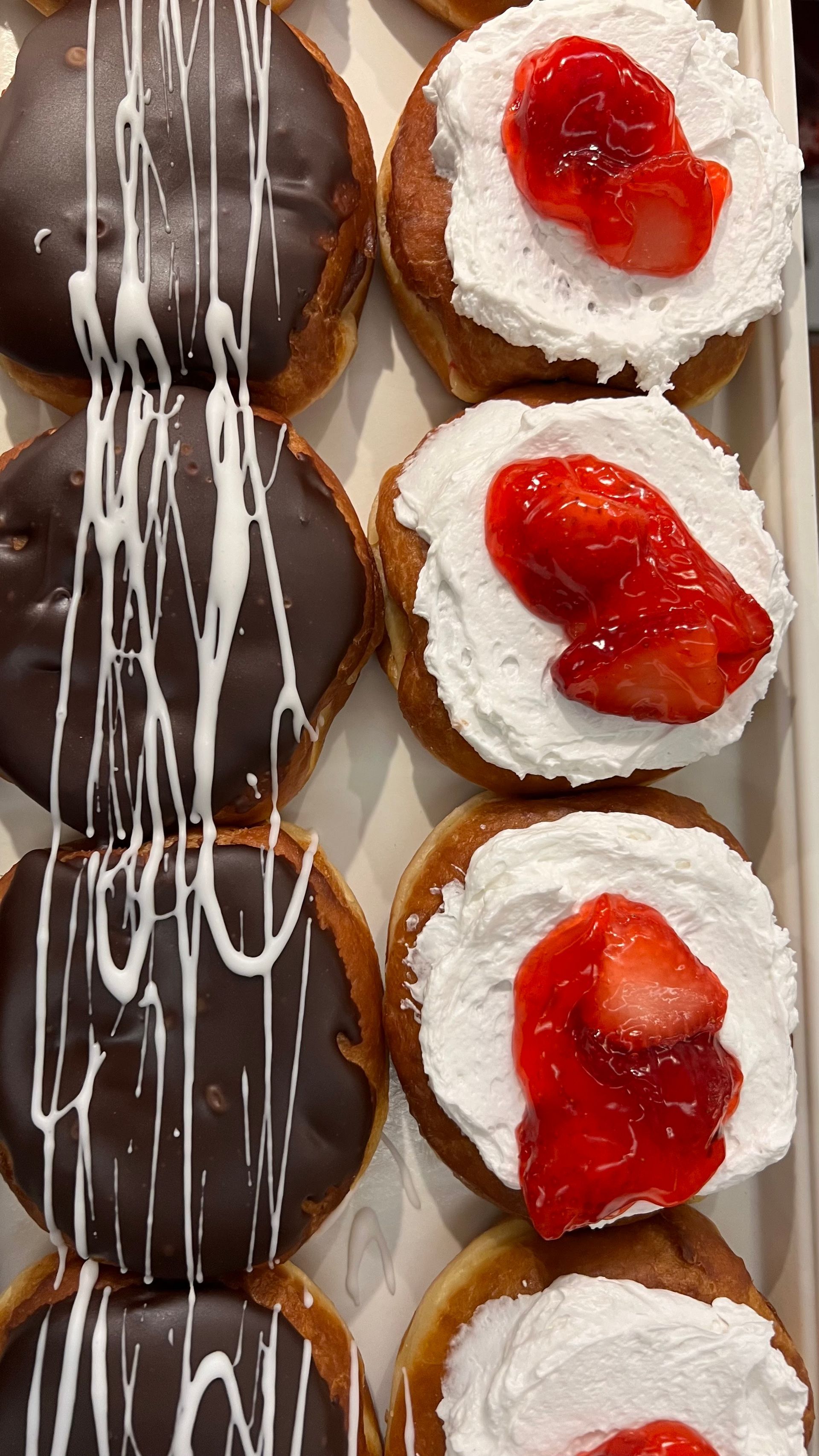 A tray of donuts with chocolate frosting and strawberries on top.
