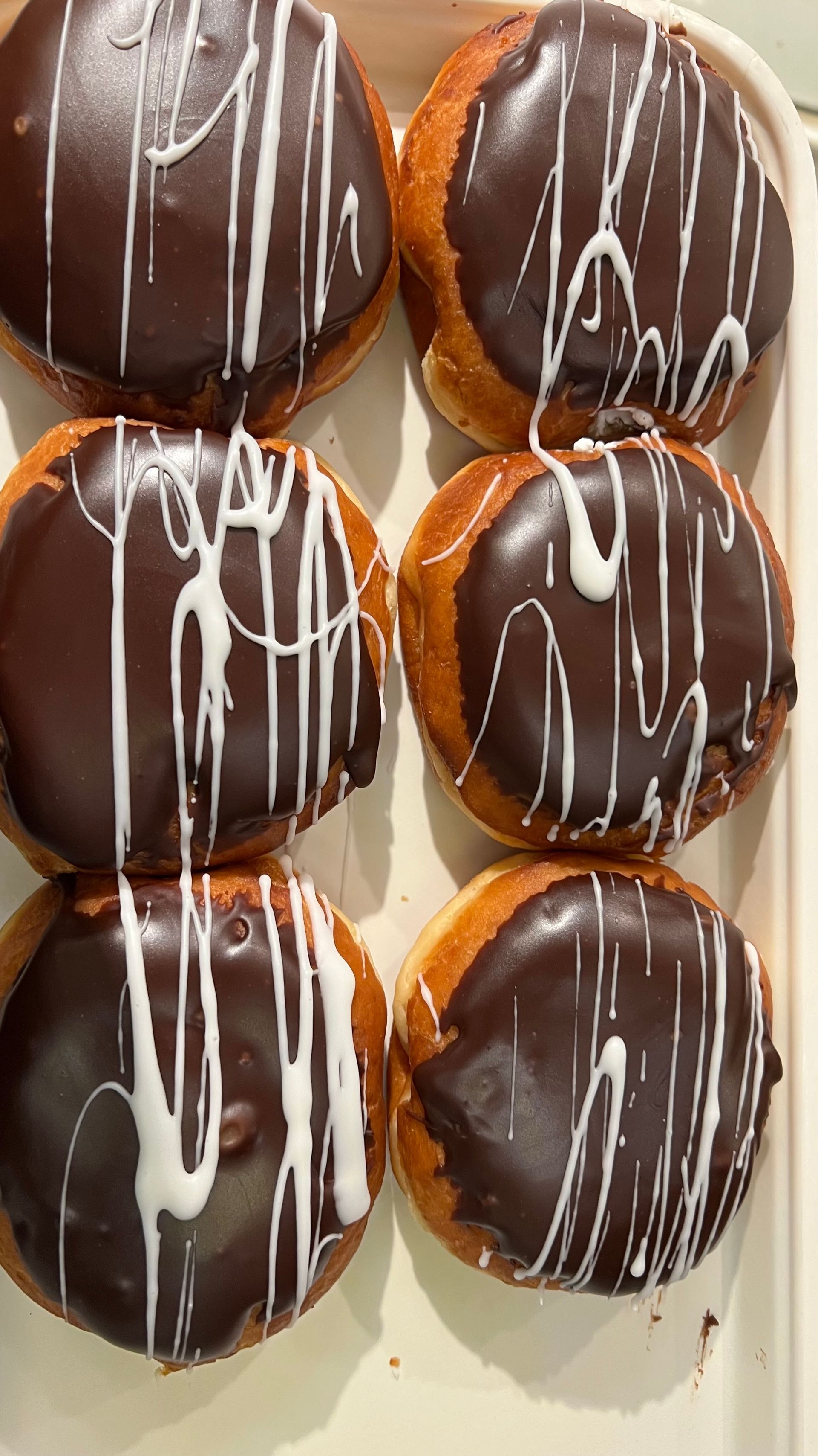 A tray of chocolate covered donuts with white frosting on a table.