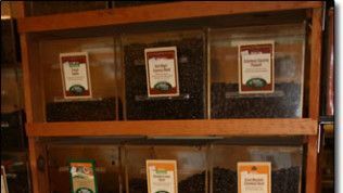 Three containers of coffee beans are sitting on a wooden shelf.