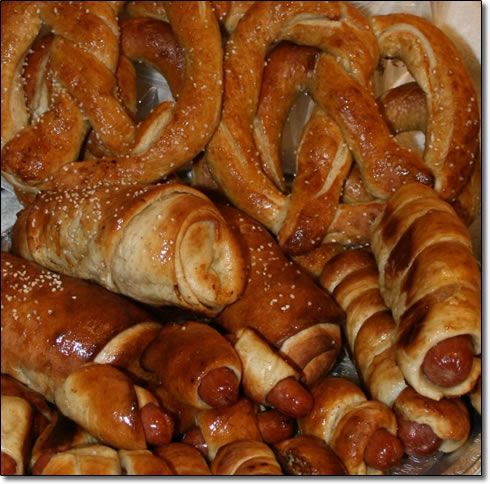A pile of pretzels and sausage rolls with sesame seeds on them