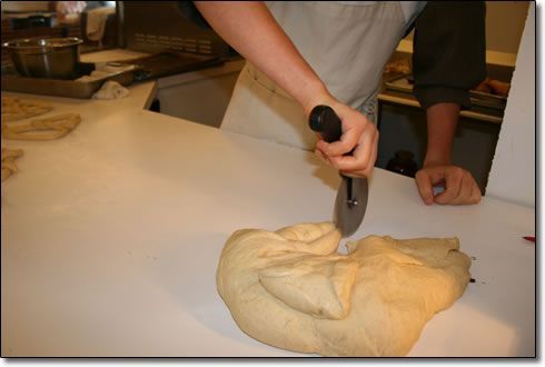 A person is cutting a piece of dough with a pizza cutter
