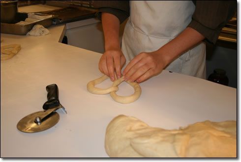 A person is making pretzels with a pizza cutter in the background