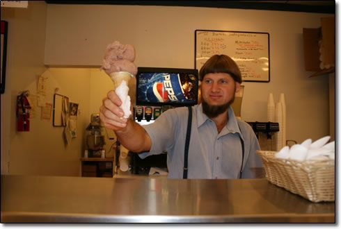 A man is holding an ice cream cone in front of a pepsi machine.